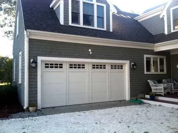Gray house exterior with white double garage doors and a gravel driveway
