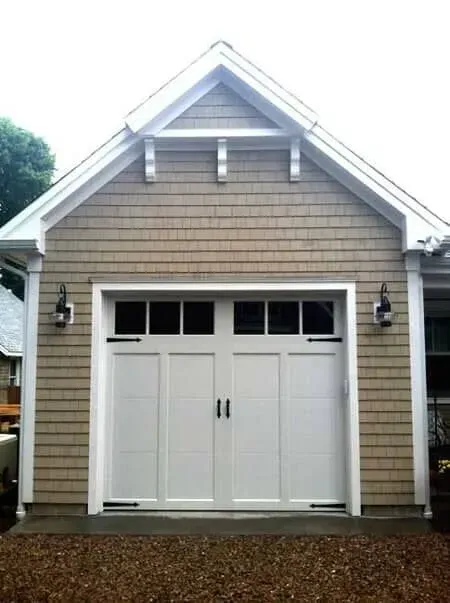 White double garage doors on a tan house with a peaked roof and wall lanterns