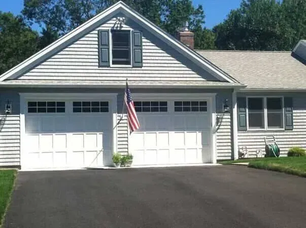Suburban house with white garage doors, black shutters, American flag, and a dark driveway