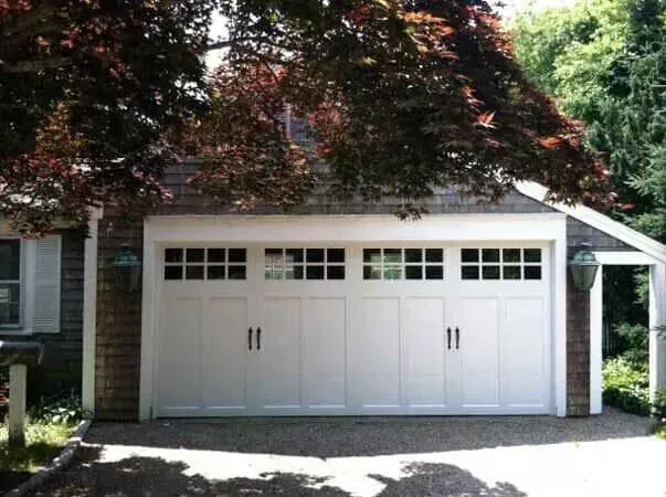 White three-car garage under trees with a driveway in front