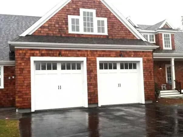 Brick house with two white garage doors and a wet driveway after rain.