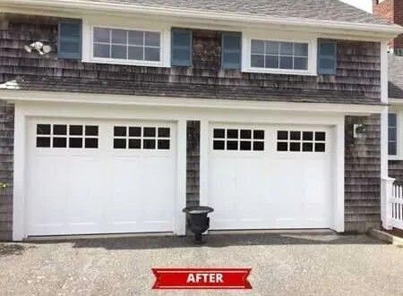 Two white garage doors on a house exterior, with a black trash bin between them