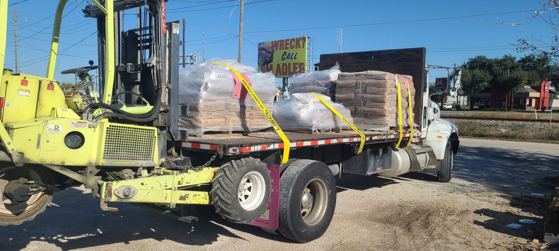 A truck with a forklift attached to it is parked in a gravel lot.