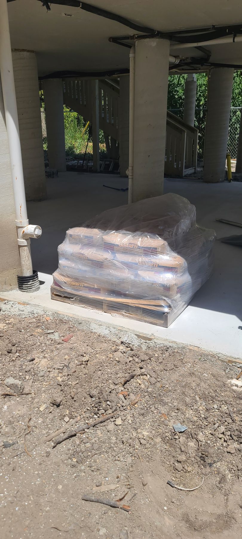 A pile of rocks wrapped in plastic is sitting on the ground in front of a building under construction.