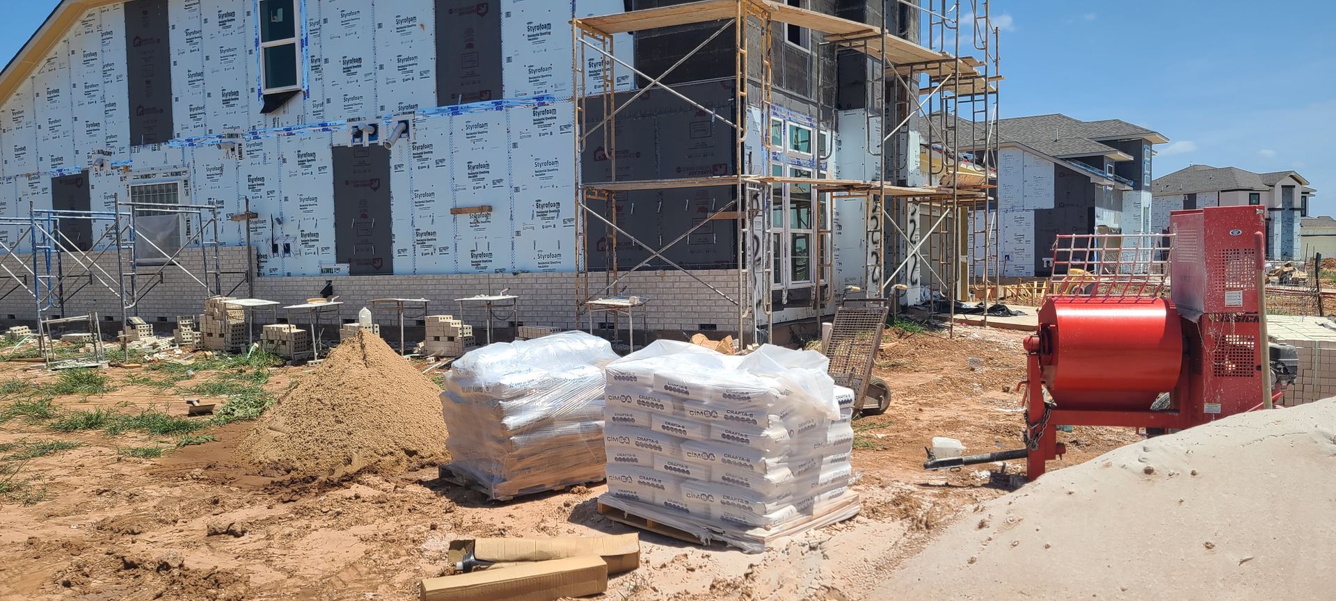 A house is being built with scaffolding and bricks in front of it.