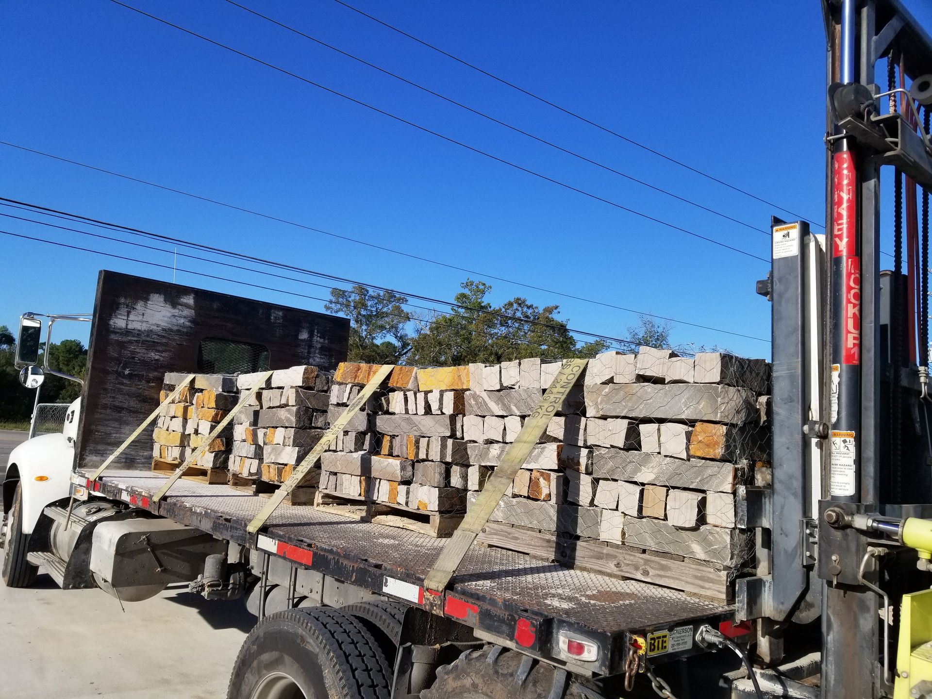 A forklift is loading bricks on the back of a semi truck.