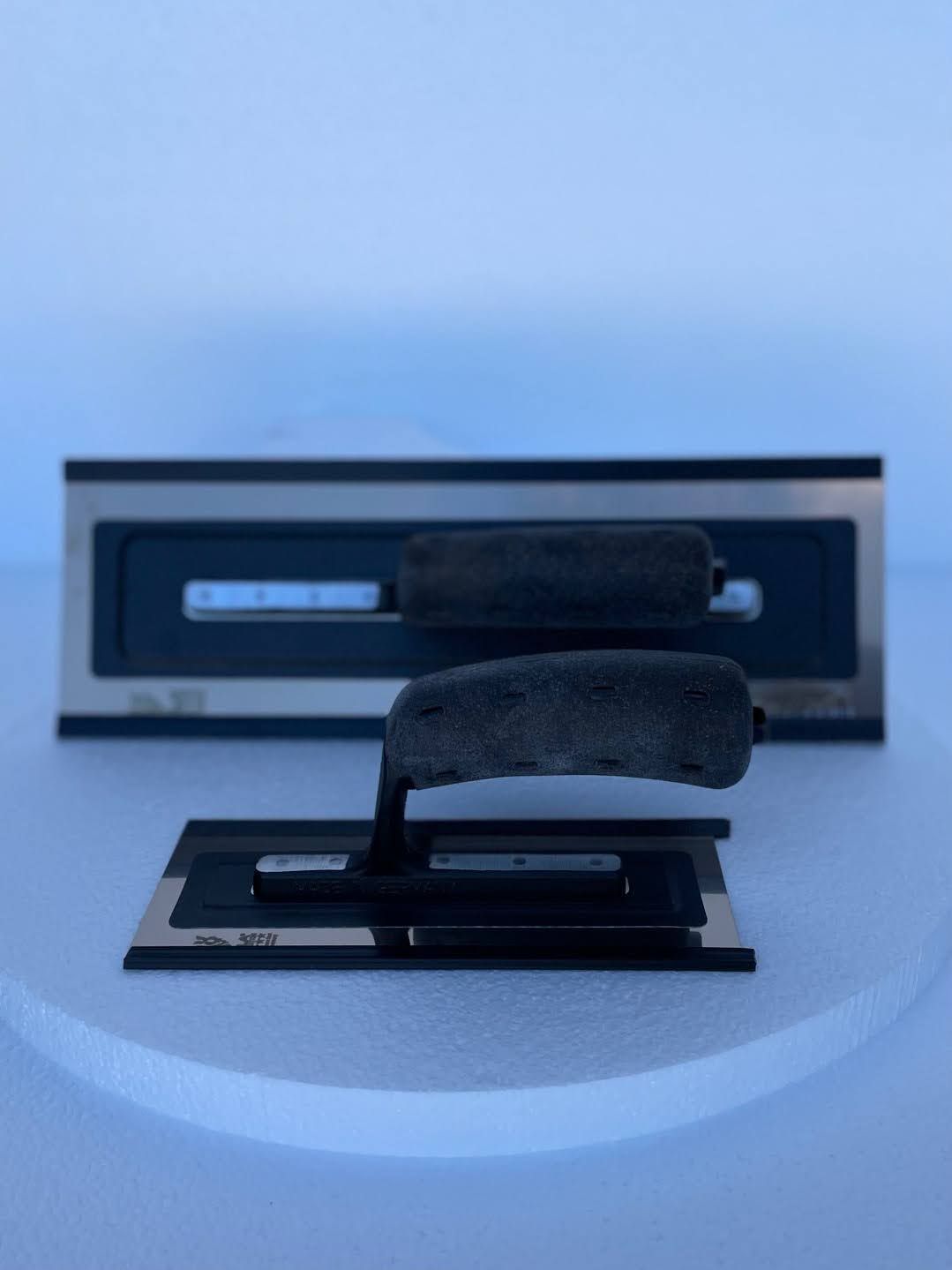 A black trowel is sitting on top of a white surface.
