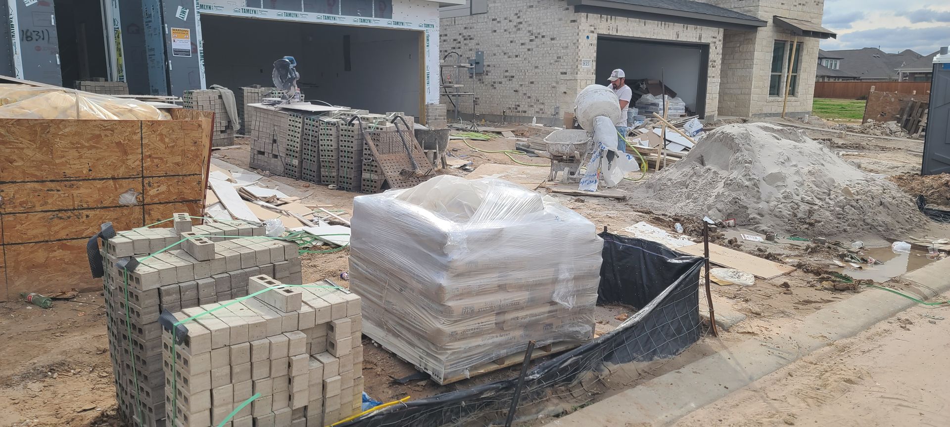 A pile of bricks is sitting on the ground in front of a house under construction.