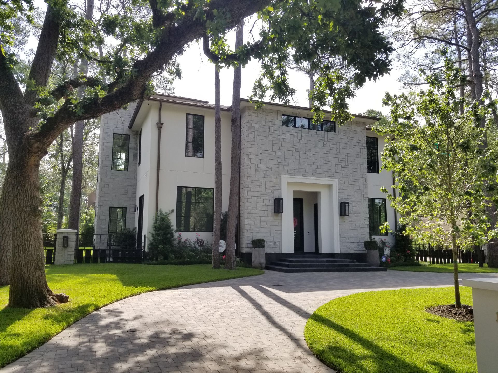 A large white house with a driveway leading to it is surrounded by trees.