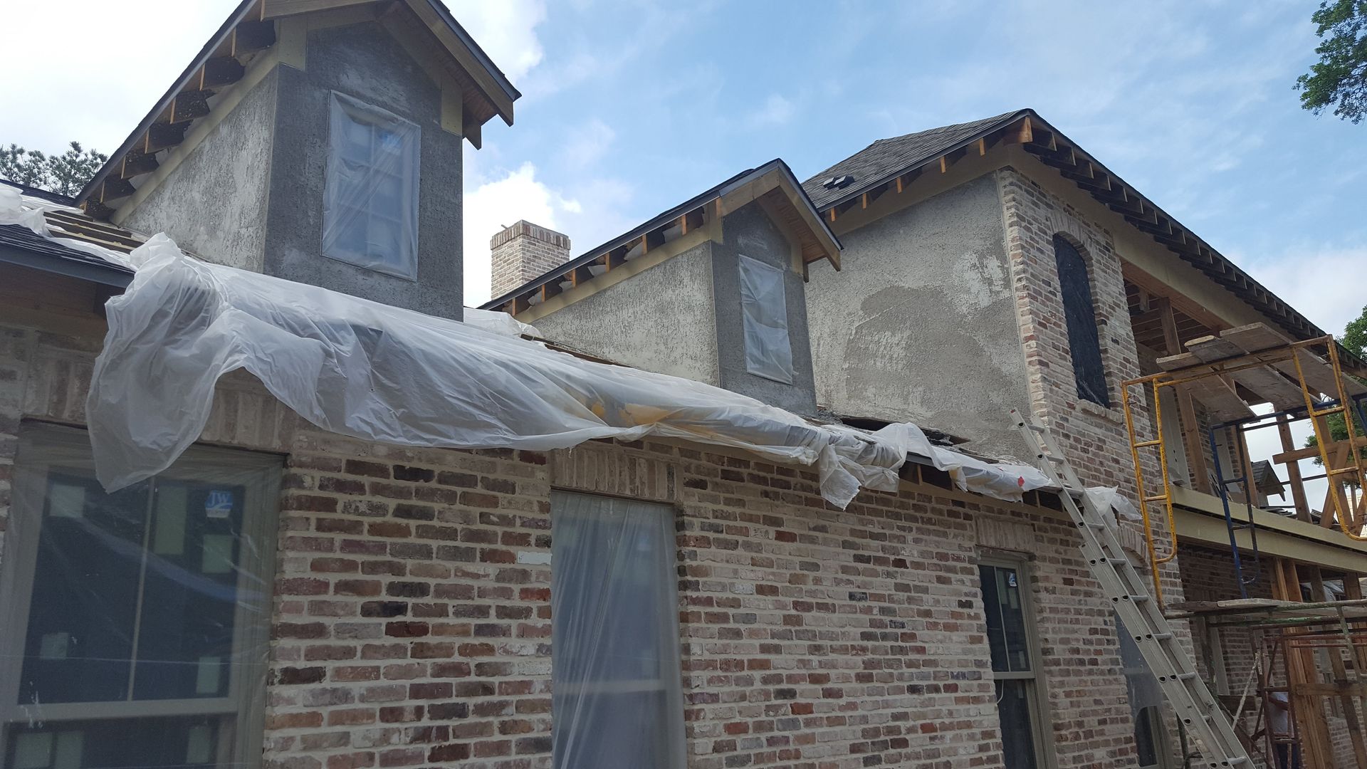 A brick house is being built with plastic wrap on the roof.