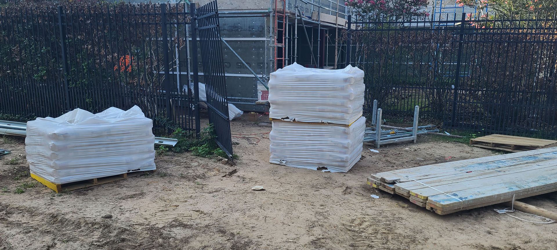 A pile of bricks sitting on top of a dirt field next to a fence.