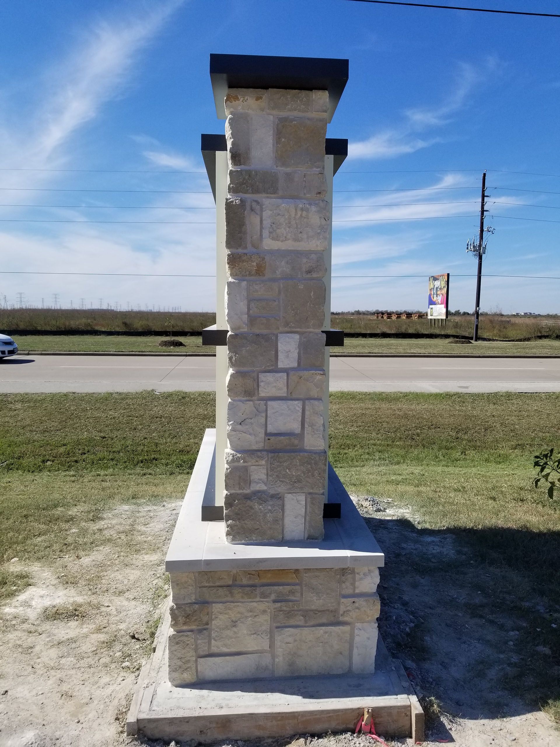 A stone pillar is sitting in the grass next to a road.