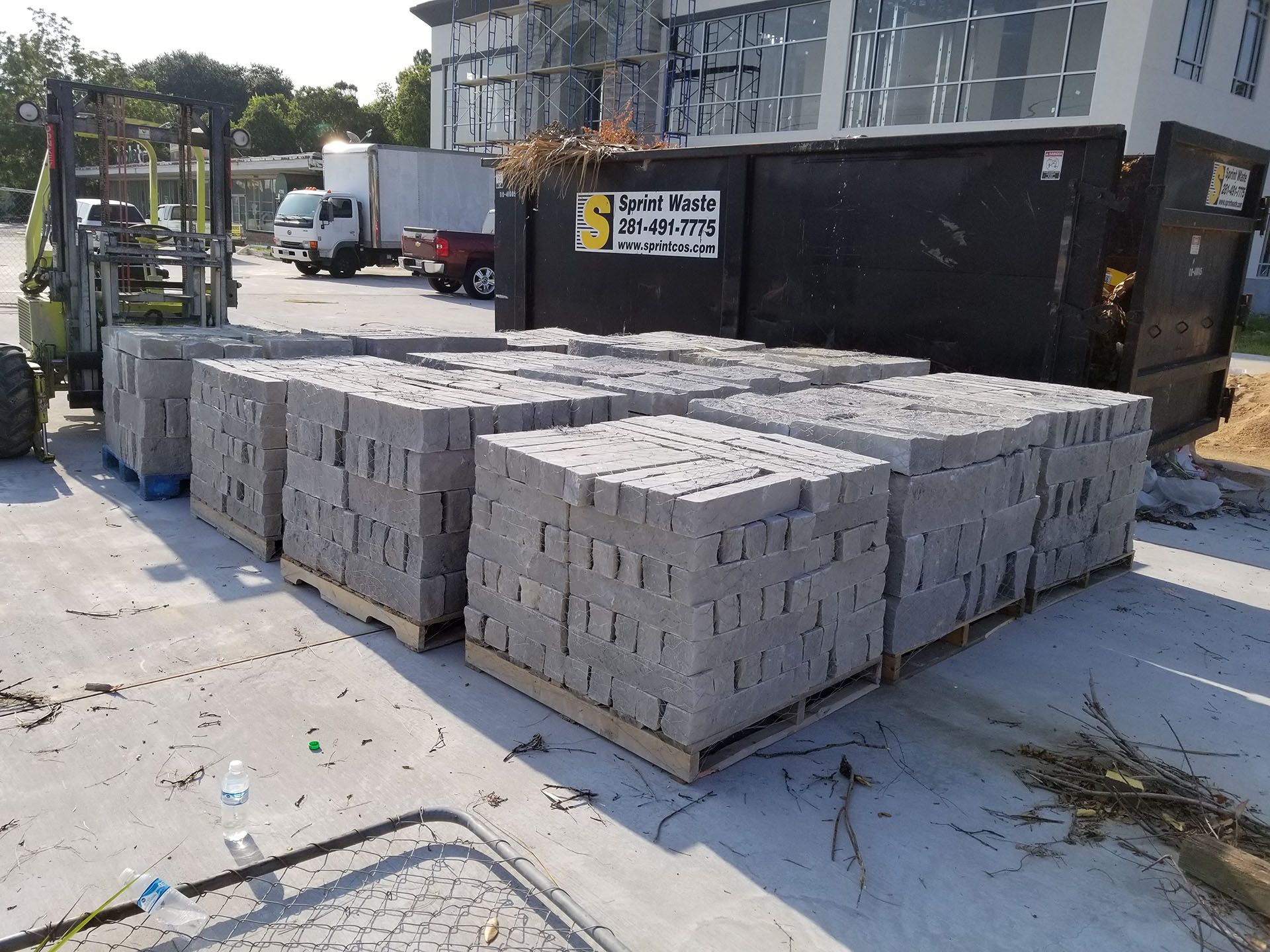 A pallet of bricks is sitting in front of a dumpster.