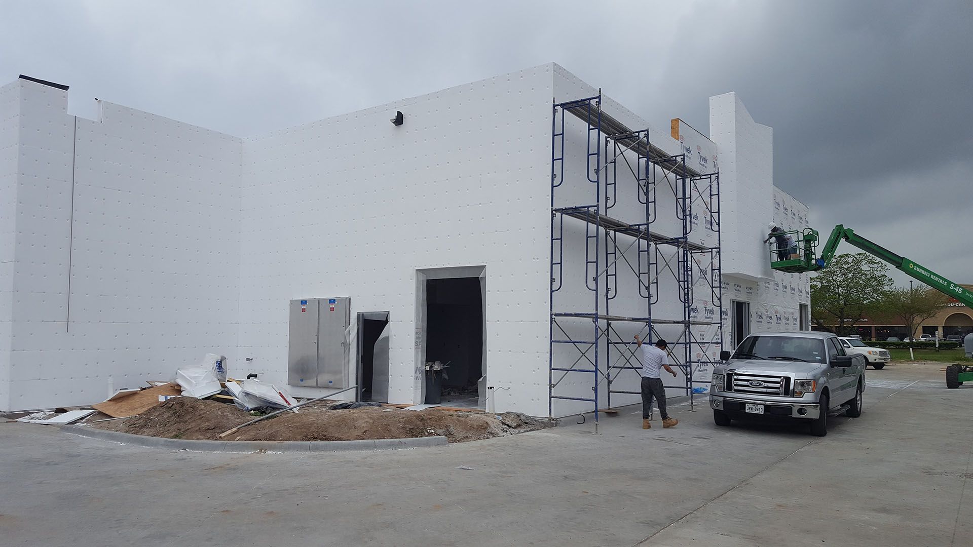 A white truck is parked in front of a building under construction.