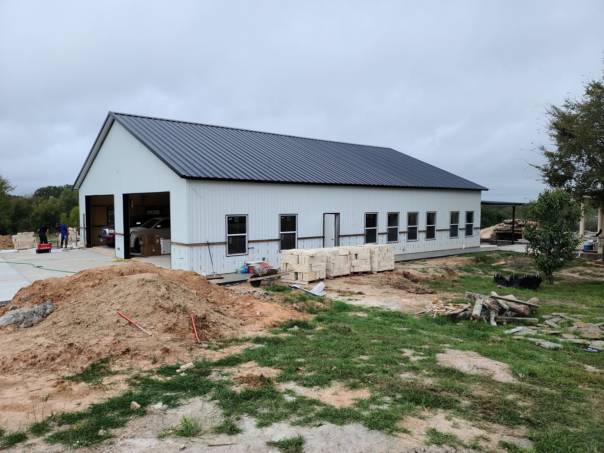 A large white barn with a black roof is being built in a field.