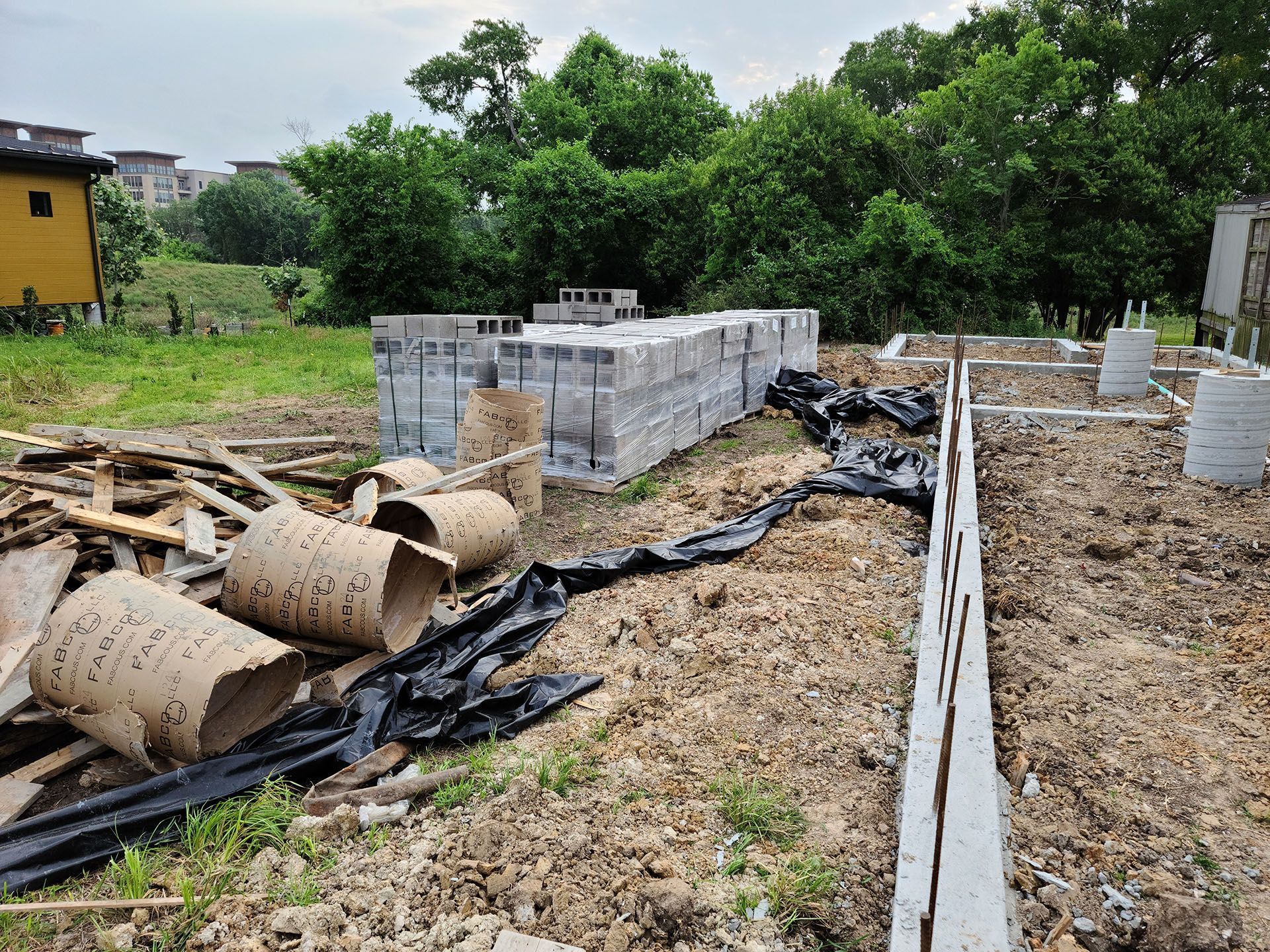 A construction site with a lot of bricks and pipes in the dirt.