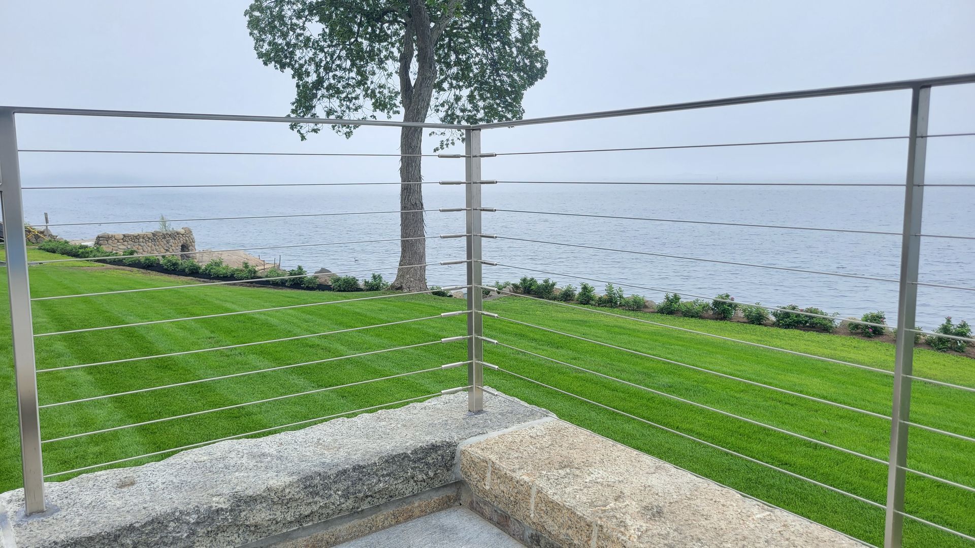 A stainless steel railing overlooking a lush green field and the ocean.