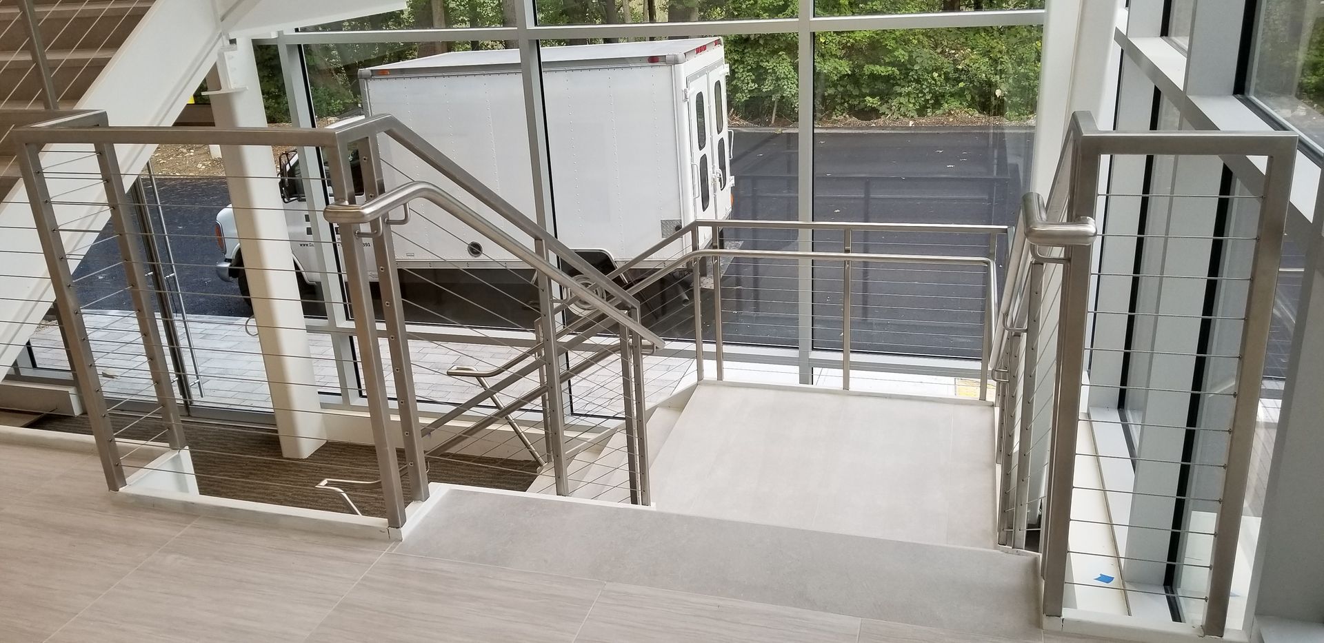 A staircase with a stainless steel railing and a white truck in the background.
