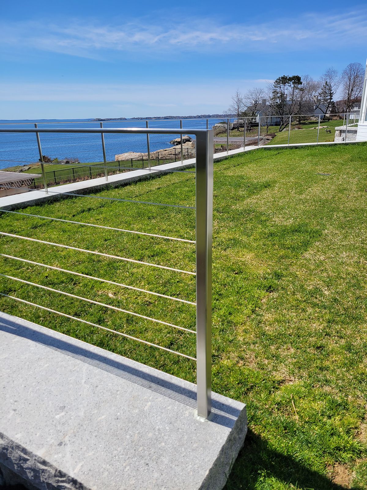 A stainless steel railing overlooking a lush green field with a view of the ocean.