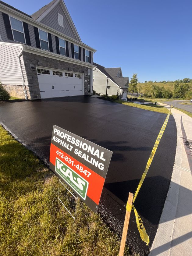 Freshly sealed black driveway beside a house, with a professional asphalt sealing sign and yellow tape.
