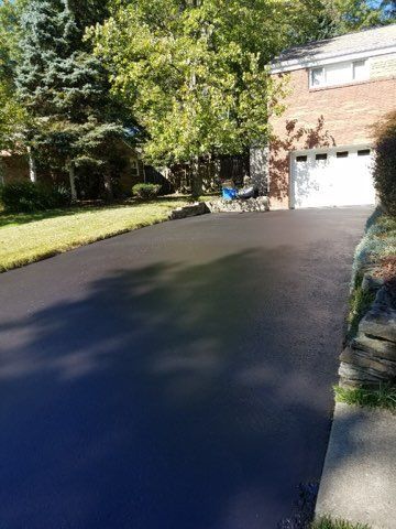 Tree-lined driveway leading to a brick house with a garage in bright sunlight