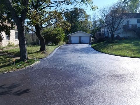 Curved paved driveway leading to a white garage in a leafy residential neighborhood