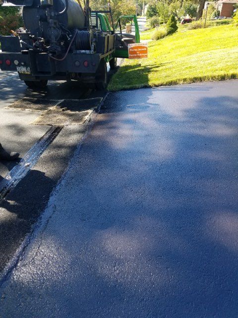 Street sweeper cleaning the edge of a sunlit road beside a grassy slope