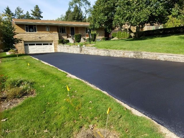 Suburban house with a newly paved black driveway and green lawn on a sunny day