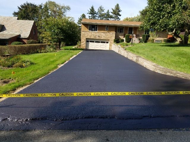 New asphalt driveway leading to a house, blocked by yellow caution tape across the bottom.