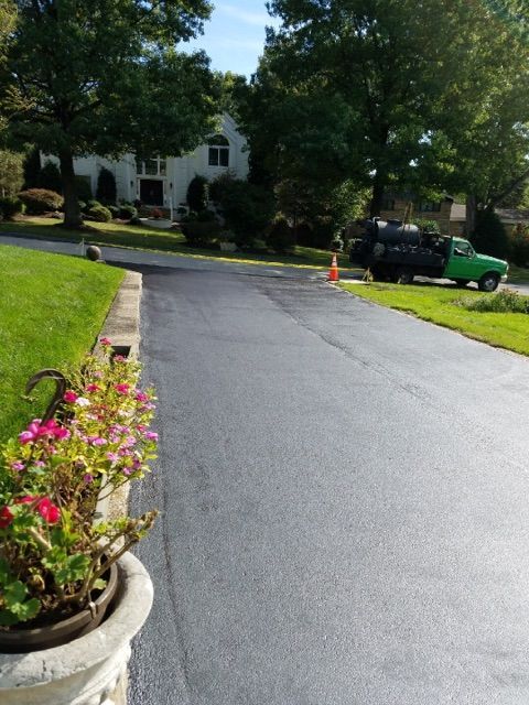 Curved driveway beside a white house, with potted flowers in the foreground and a green pickup truck parked nearby.
