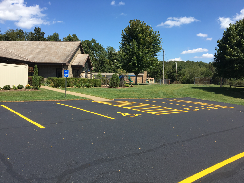 Empty parking lot with yellow lines beside a brick building and trees under a blue sky