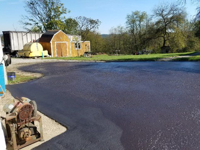 Freshly paved driveway beside a small shed and grassy yard on a sunny day