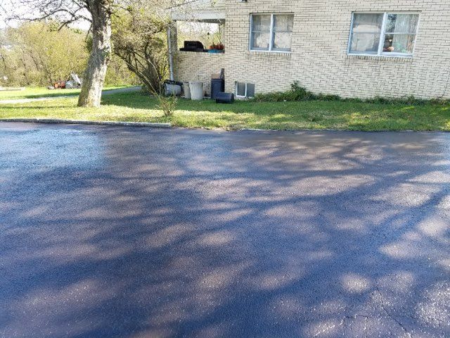 Driveway beside a white house with windows, tree shadows across the pavement