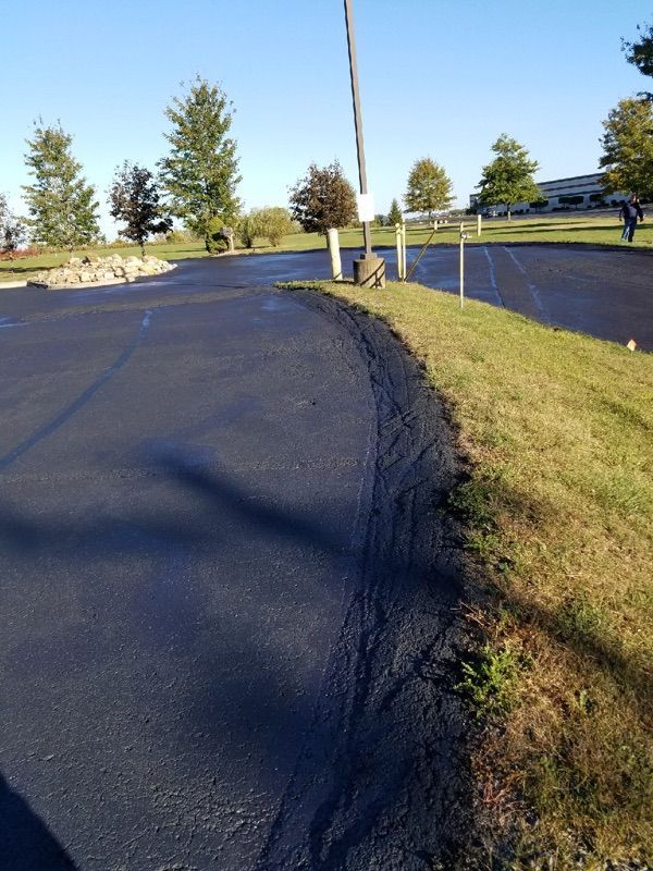 Curved asphalt path beside a grassy edge in a park with trees and a fence at sunset