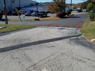 Empty parking lot with orange cones blocking a cracked asphalt driveway near buildings