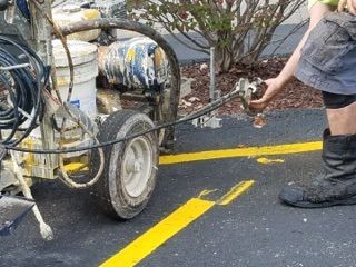 Worker spraying a road barrier from a small cart beside yellow lane markings