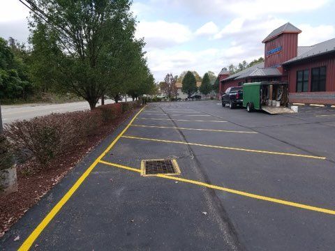 Empty parking lot with yellow lines, a drain grate, and a building beside trees.