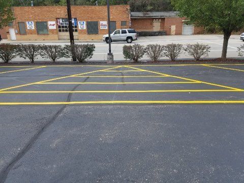 Empty parking lot with yellow crosshatched lines in front of a brick building and parked white car.