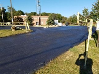Newly paved road curving through a fenced, grassy area on a sunny day