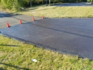 Freshly paved road section marked by orange traffic cones along a grassy roadside.