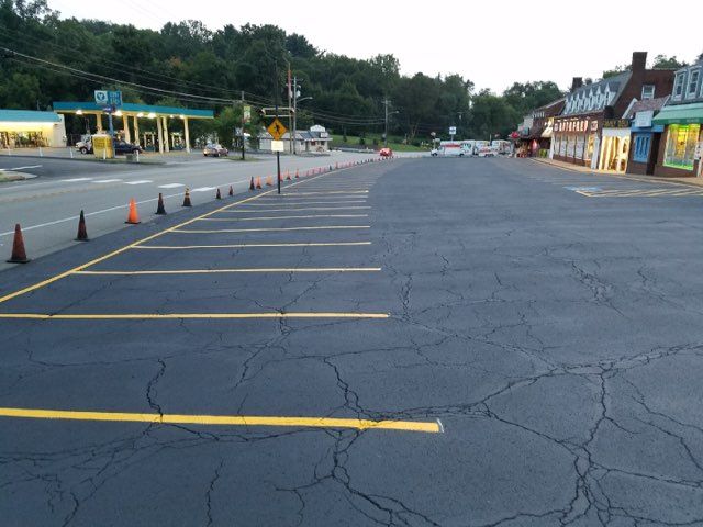 Empty parking lot with yellow lines, orange cones, and roadside shops at dusk