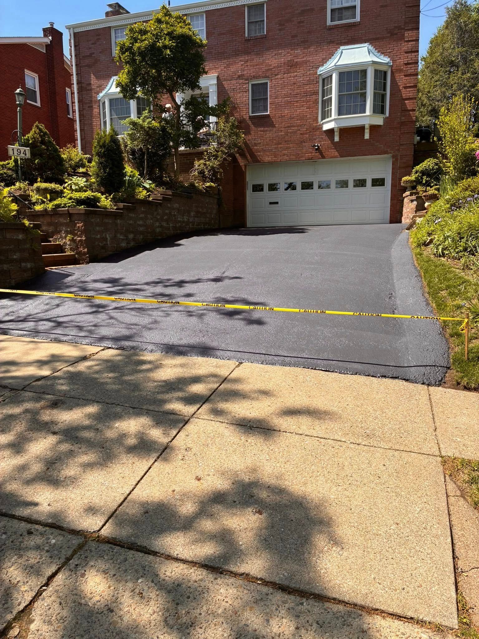 Brick house with garage, sloped asphalt driveway, and yellow caution tape across the entrance.