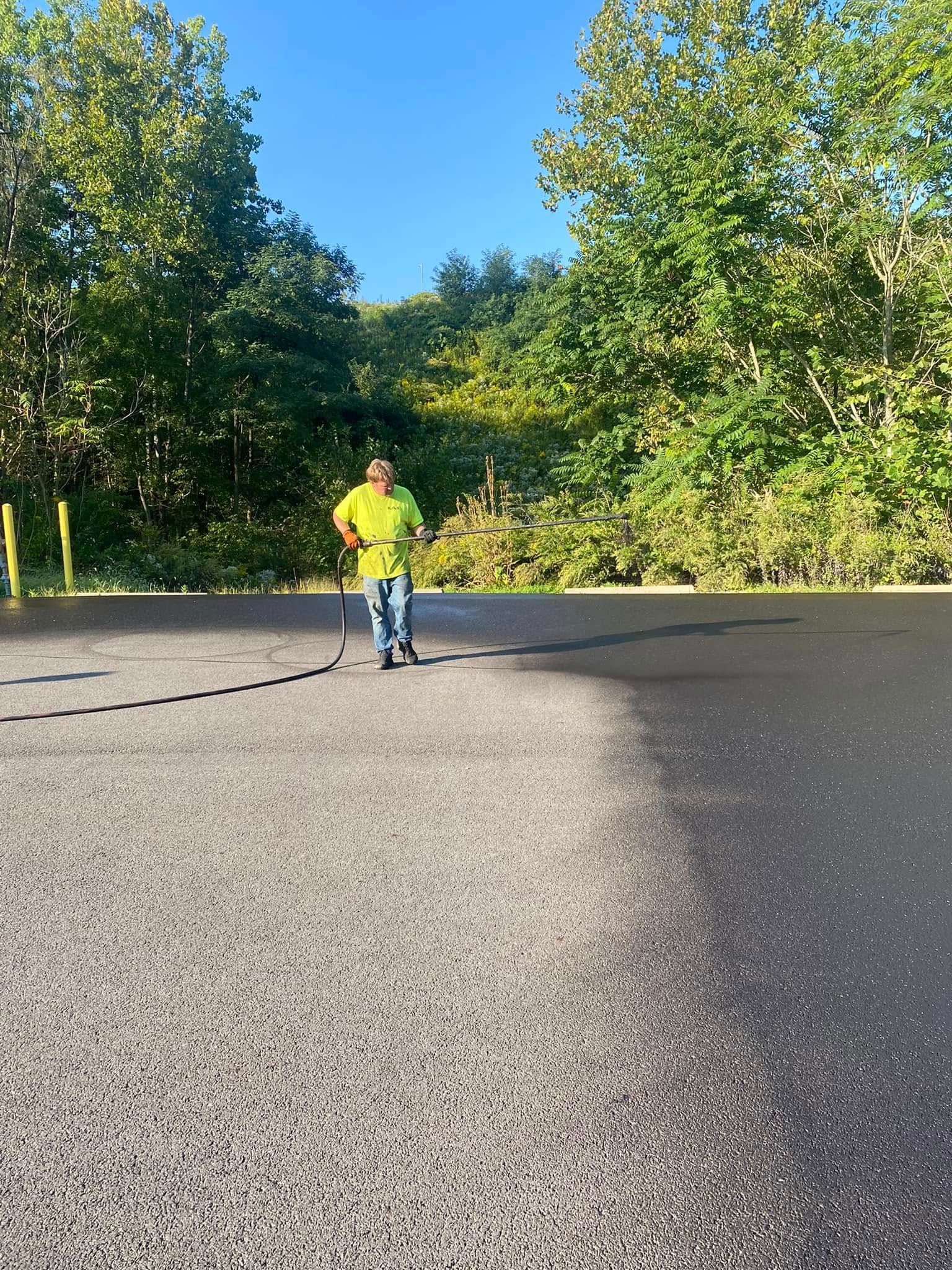Person in a neon yellow jacket walking across an empty paved road beside trees on a sunny day