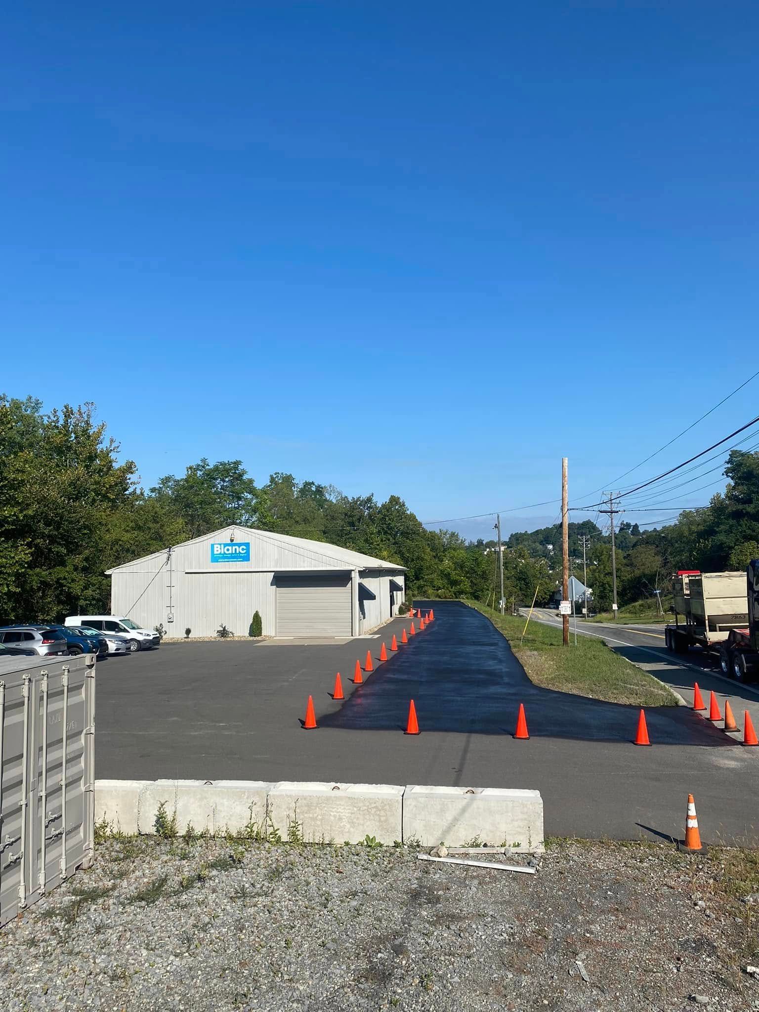 Parking lot with orange cones and a fresh black paved strip leading to a beige building under a blue sky