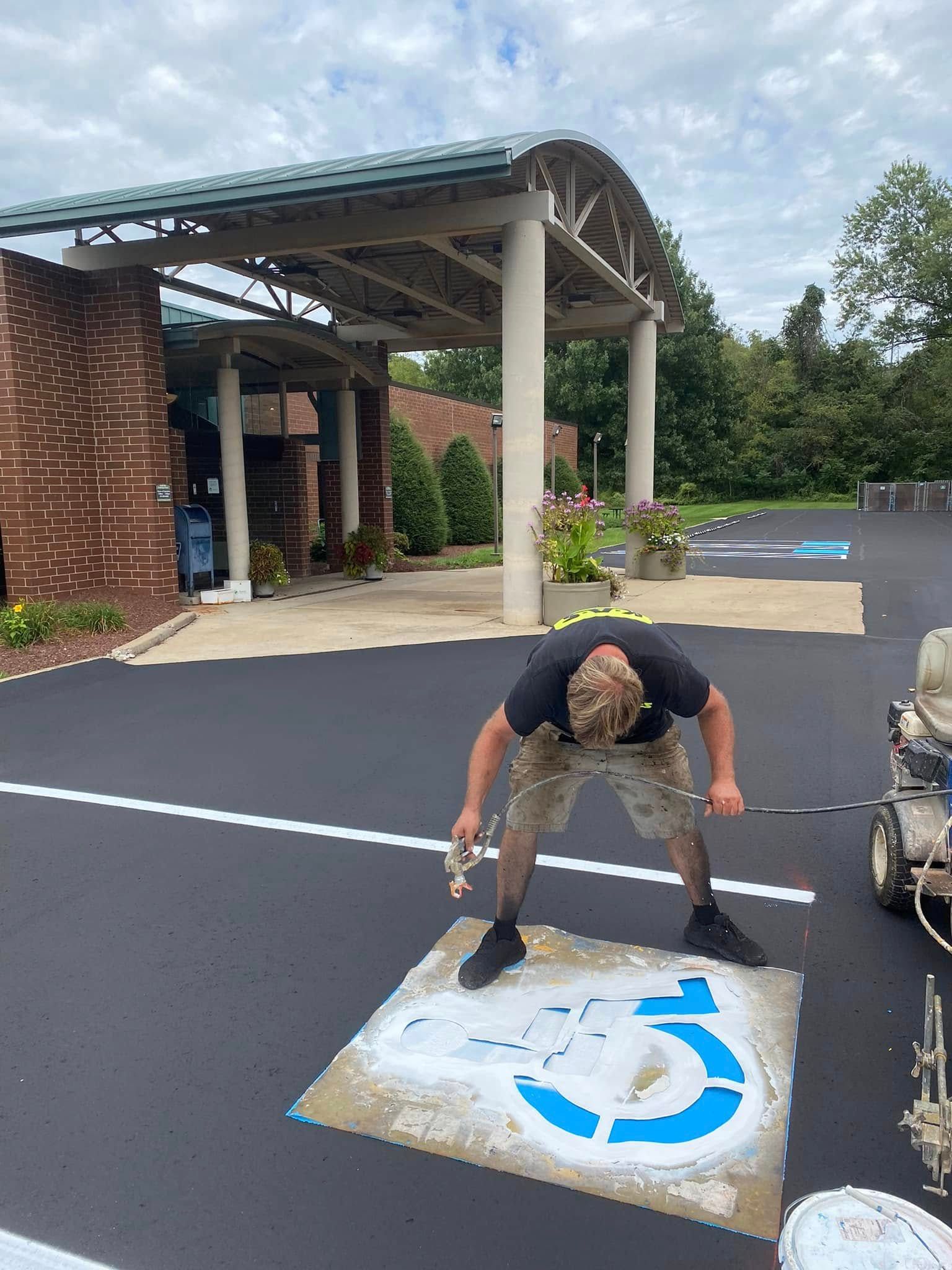 Man painting a blue wheelchair-accessible symbol on asphalt outside a building