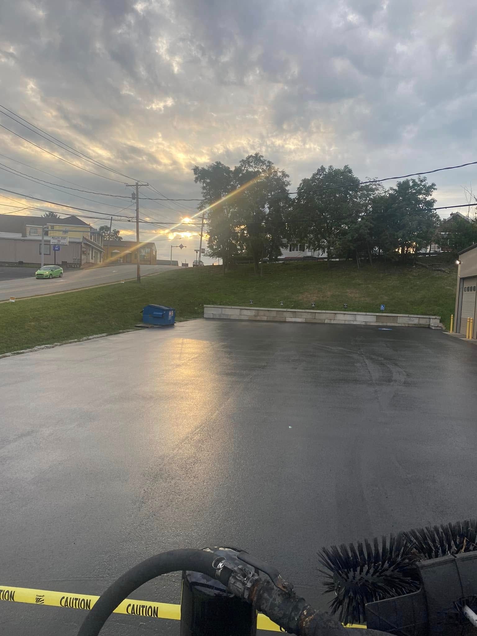 Rain-soaked parking lot at sunset with wet pavement, cloudy sky, and yellow caution tape in the foreground