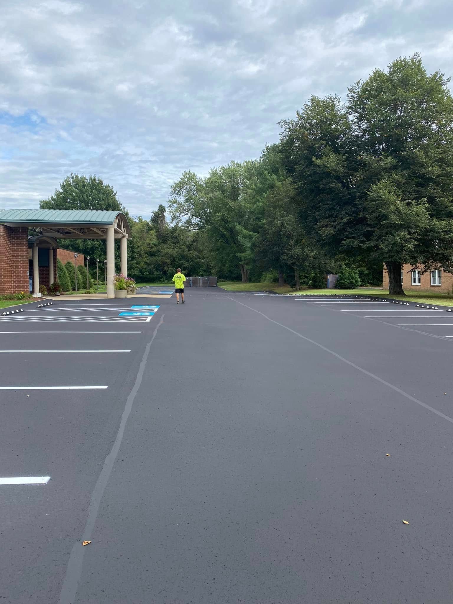 Empty parking lot beside a brick building, with a person in a yellow jacket near the entrance.