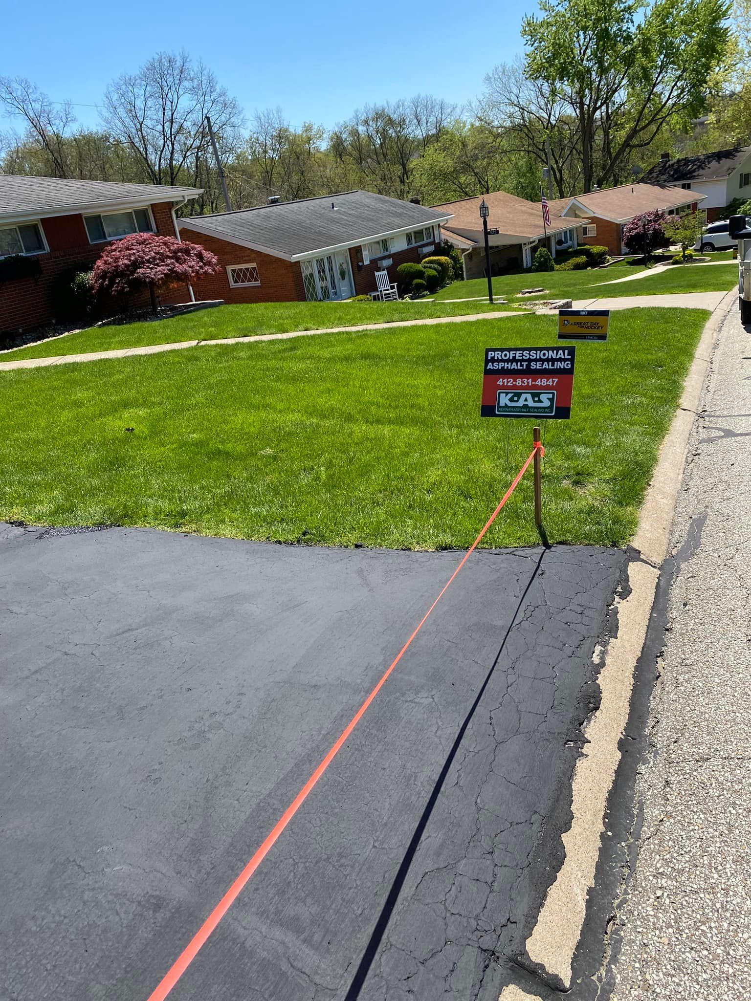 Front lawn with a small yard sign, orange cord, and suburban houses along a sidewalk.
