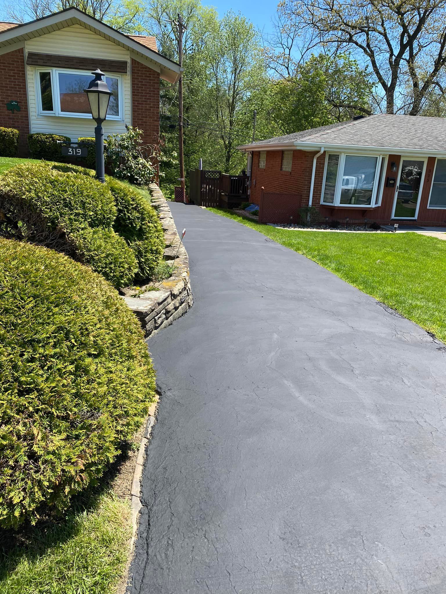 Curved blacktop driveway between brick buildings and trimmed hedges on a sunny day