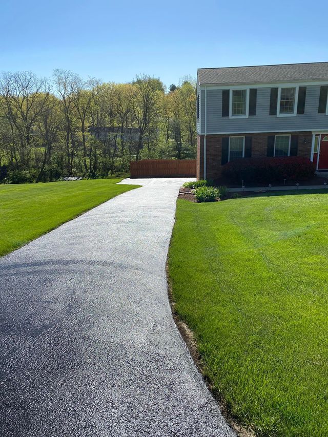 Gravel driveway leading to a two-story house with a green lawn and trees in the background
